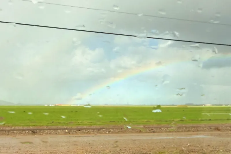 A rainbow arcs over green fields under gray rain clouds